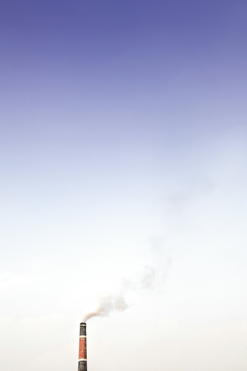 Un camino industriale a strisce rilascia fumo bianco nel cielo.