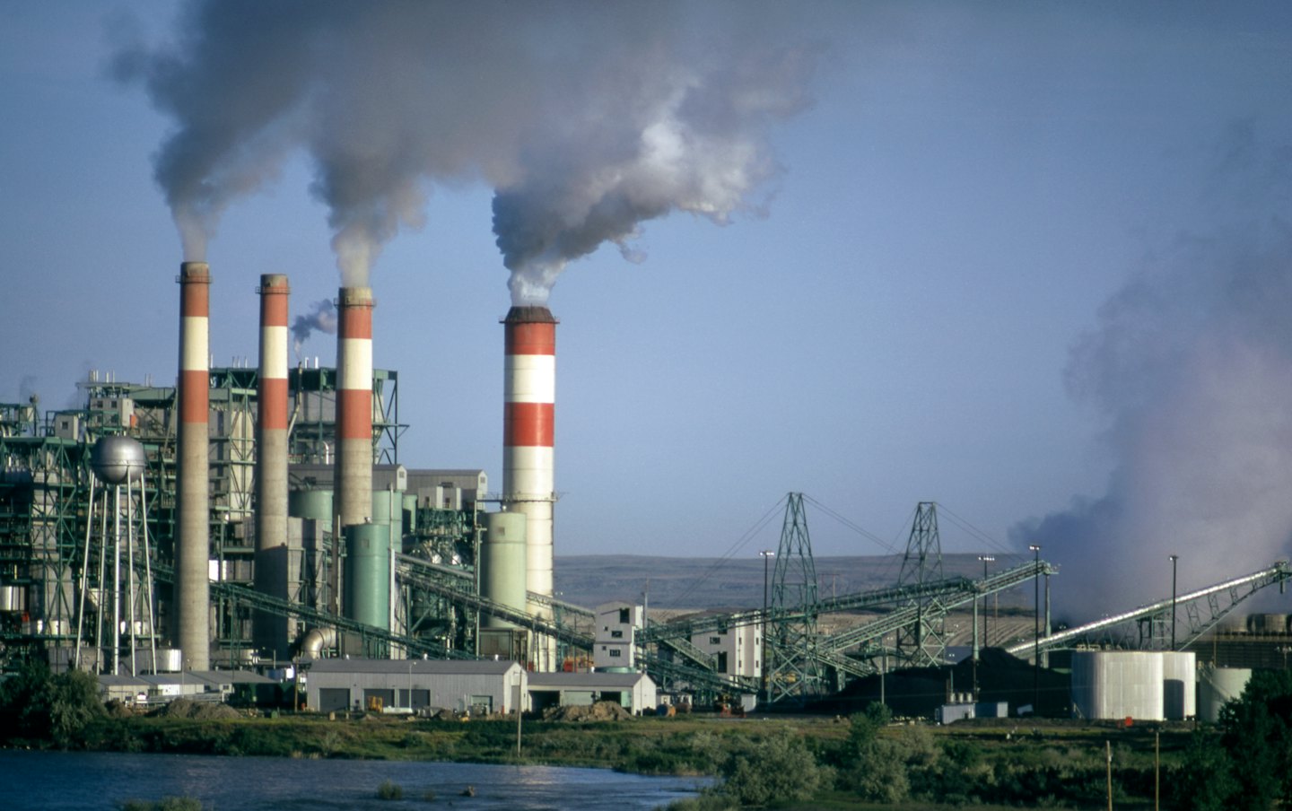 Centrale elettrica industriale con ciminiere che rilasciano vapore vicino all'acqua.