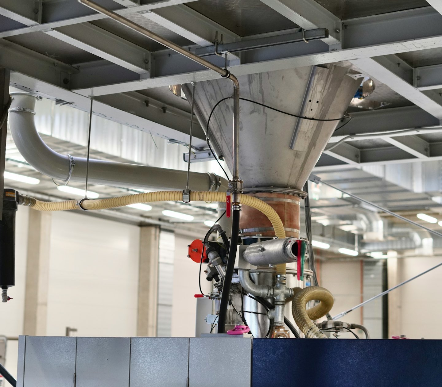 Sistema industriale di tramogge metalliche e tubazioni all'interno di uno stabilimento di produzione.